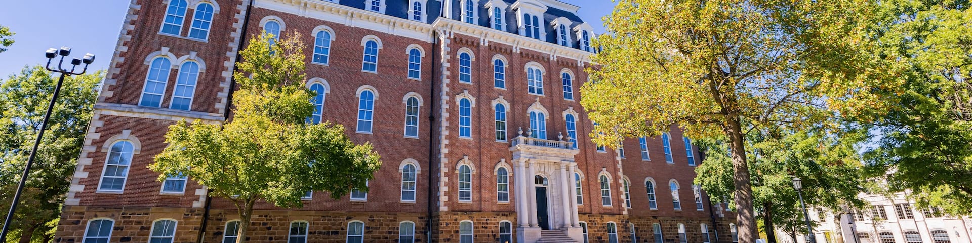 A large brick building with a clock tower, surrounded by trees and a clear blue sky.