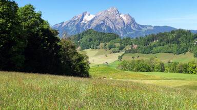 Una cordillera con un pico destacado, campos verdes exuberantes y áreas boscosas densas.