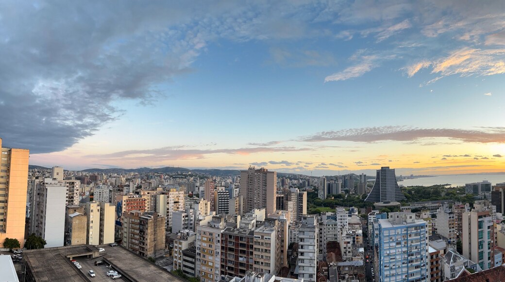 A cityscape with a sunset over a body of water, high-rise buildings, and a clear sky.