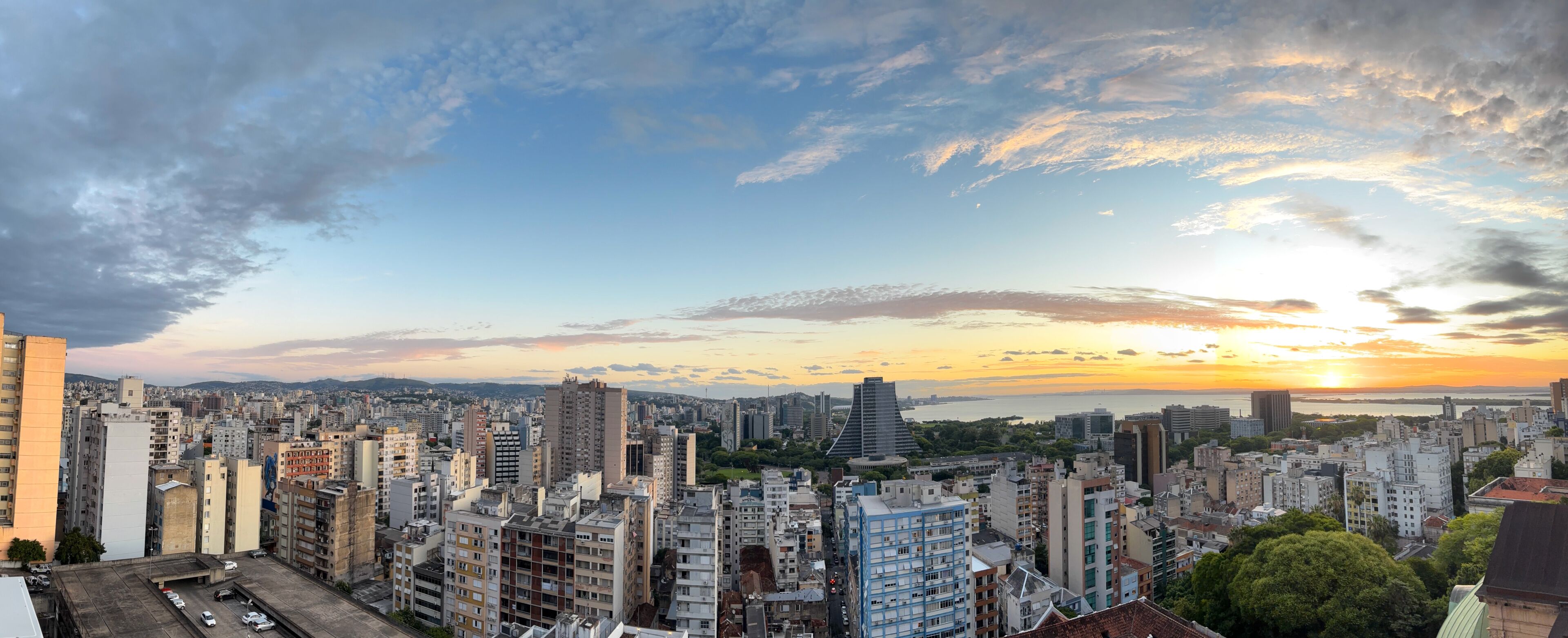 A cityscape with a sunset over a body of water, high-rise buildings, and a clear sky.
