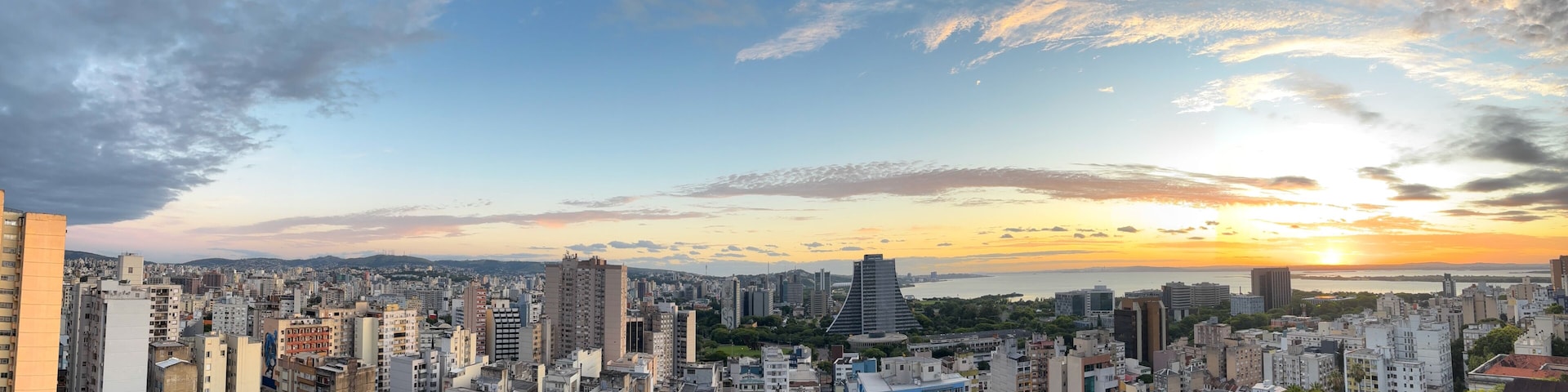A cityscape with a sunset over a body of water, high-rise buildings, and a clear sky.
