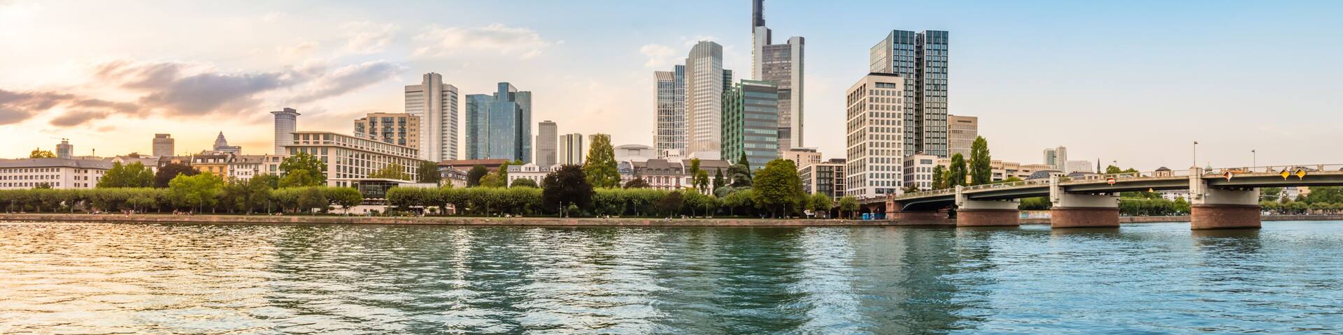 Panoramic view of Frankfurt am Main skyline with touristic boat, promenade and skyscrapers over the Main river at sunset