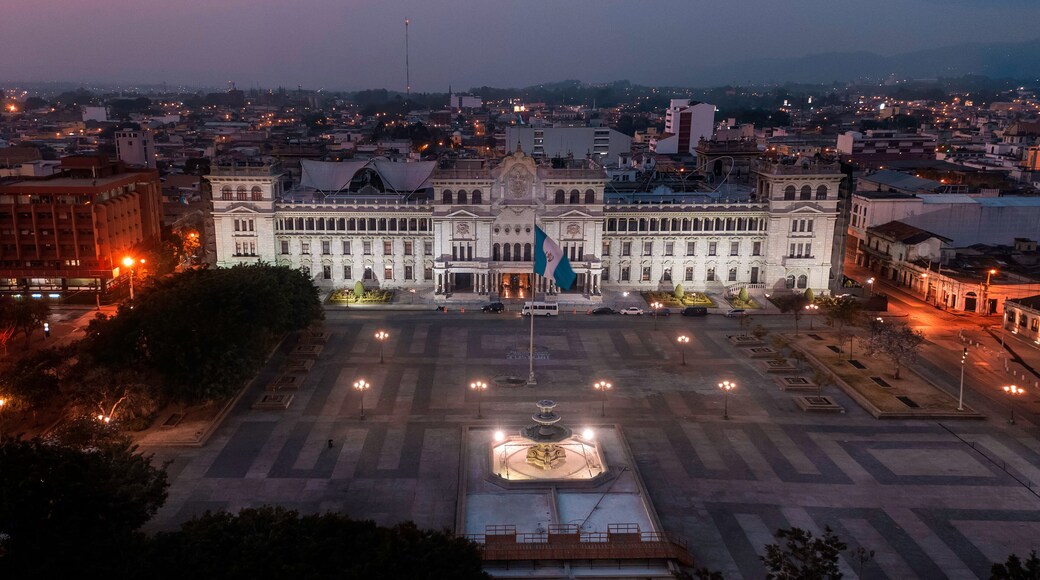 A large, historic building with a central courtyard, surrounded by a cityscape at dusk.