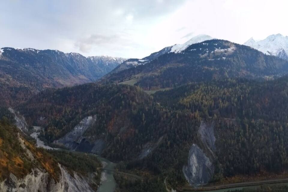 A mountainous landscape with a winding road, dense forests, and snow-capped peaks.