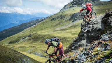 Dos ciclistas de montaña en un sendero pedregoso, con un paisaje montañoso al fondo.