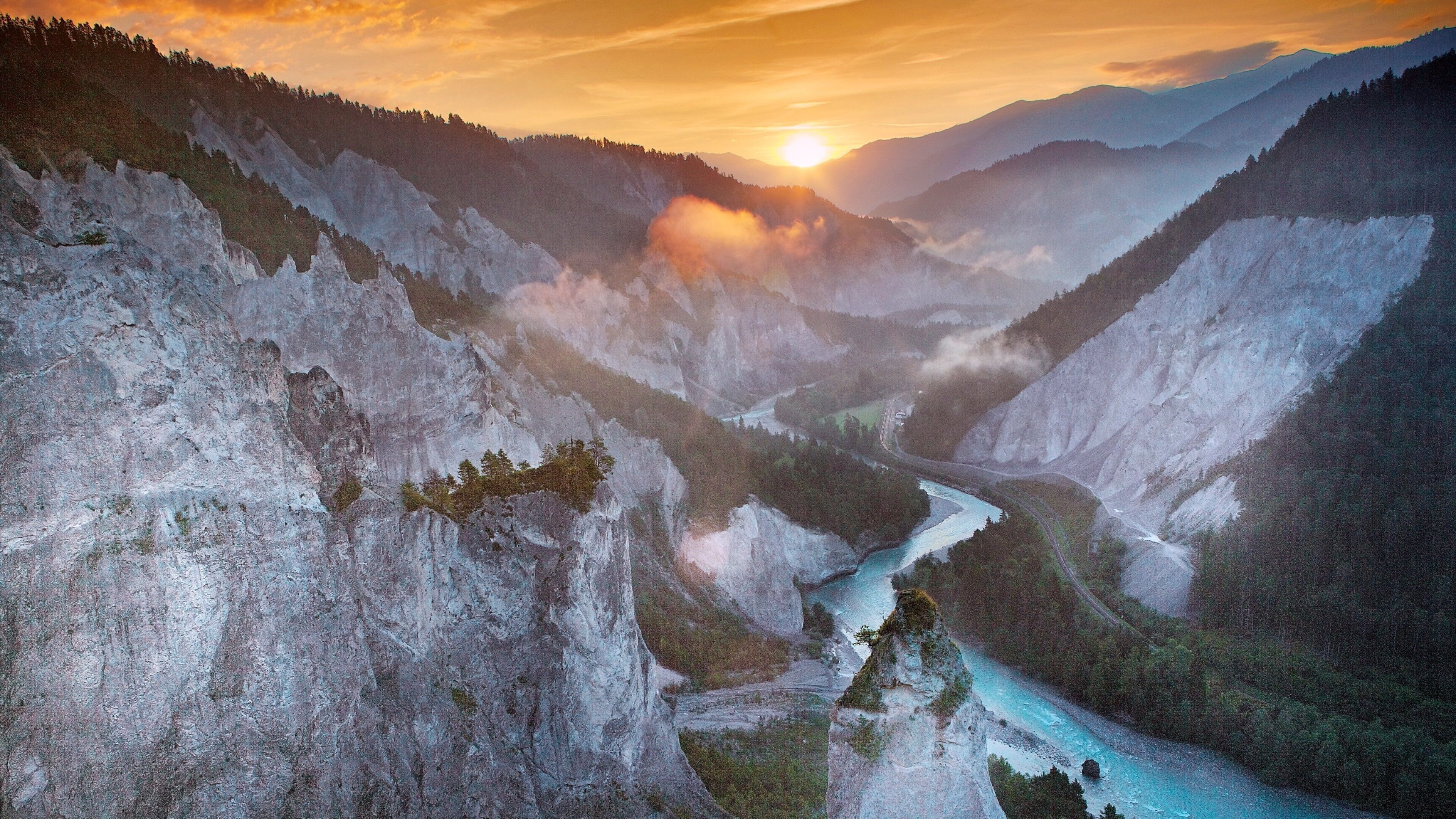 A river winding through a mountainous valley with a sunset in the background.