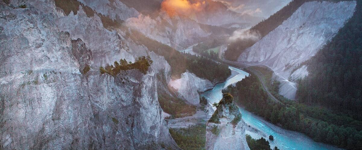 A river winding through a mountainous valley with a sunset in the background.
