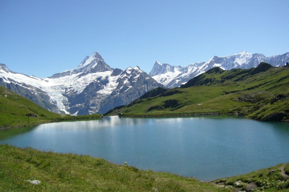 Un lago de montaña rodeado de picos nevados y colinas verdes.