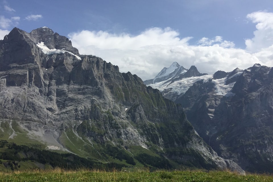 Un paysage montagneux caractérisé par des pics escarpés, des zones enneigées et une vallée où la végétation est luxuriante.