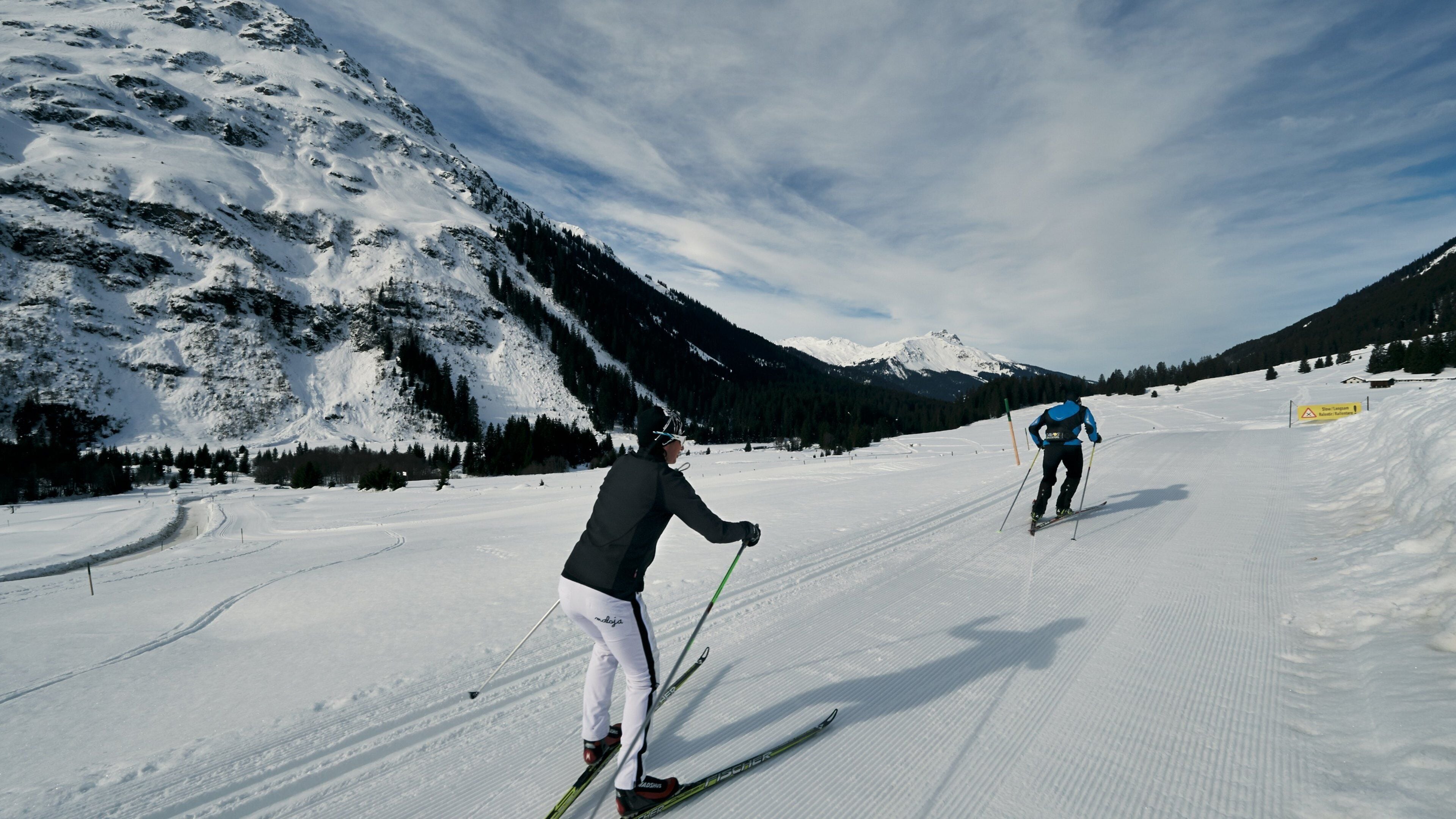 A snowy ski slope with skiers, a mountain in the background, and a clear sky.