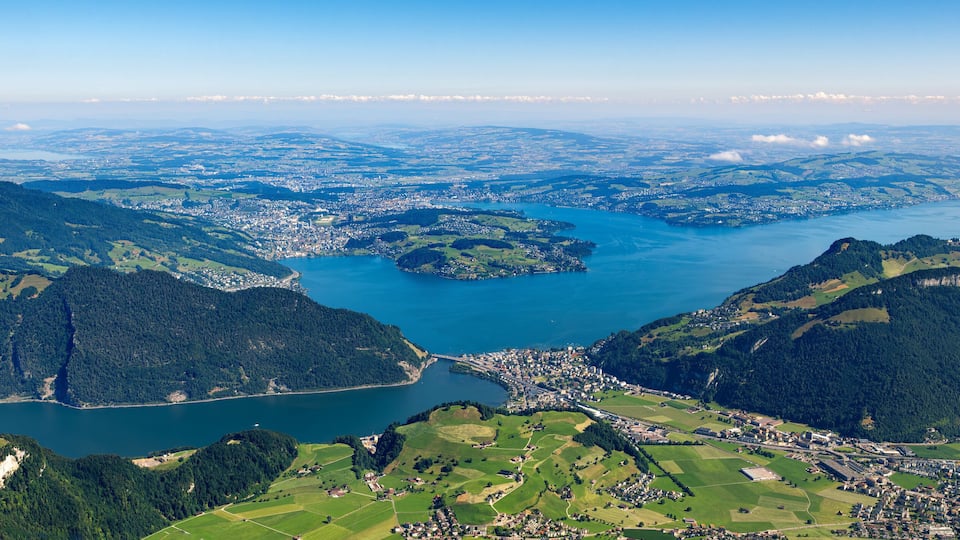 A lake surrounded by mountains, a town, and fields.