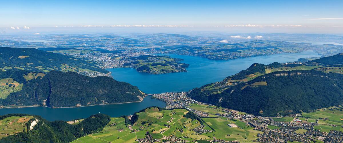 A lake surrounded by mountains, a town, and fields.