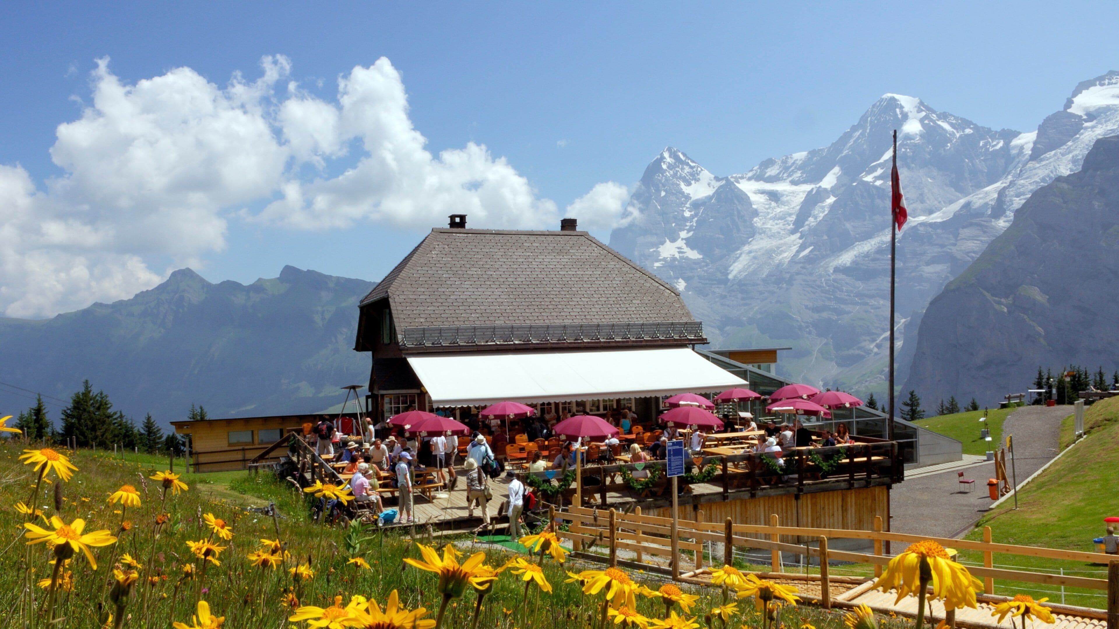 A mountain restaurant with outdoor seating and a view of snow-capped peaks.