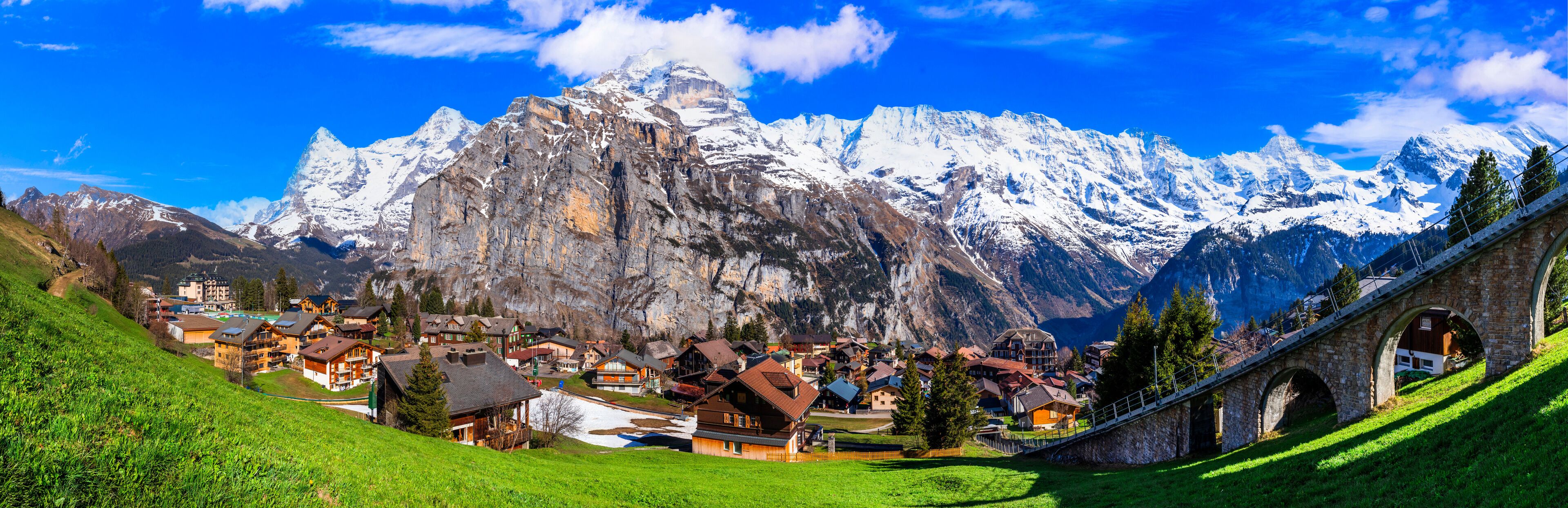 A mountain village with snow-capped peaks, a stone bridge, and traditional houses.