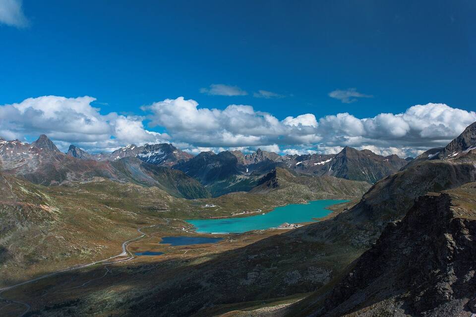 A mountainous landscape with a turquoise lake surrounded by rugged peaks and a winding road.