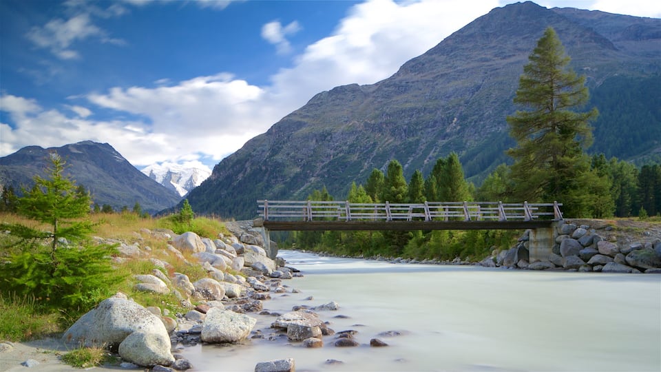 A wooden bridge over a river with mountains in the background.