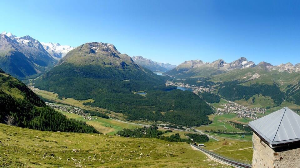 A mountainous landscape with a valley, a small town, and a clear blue sky.