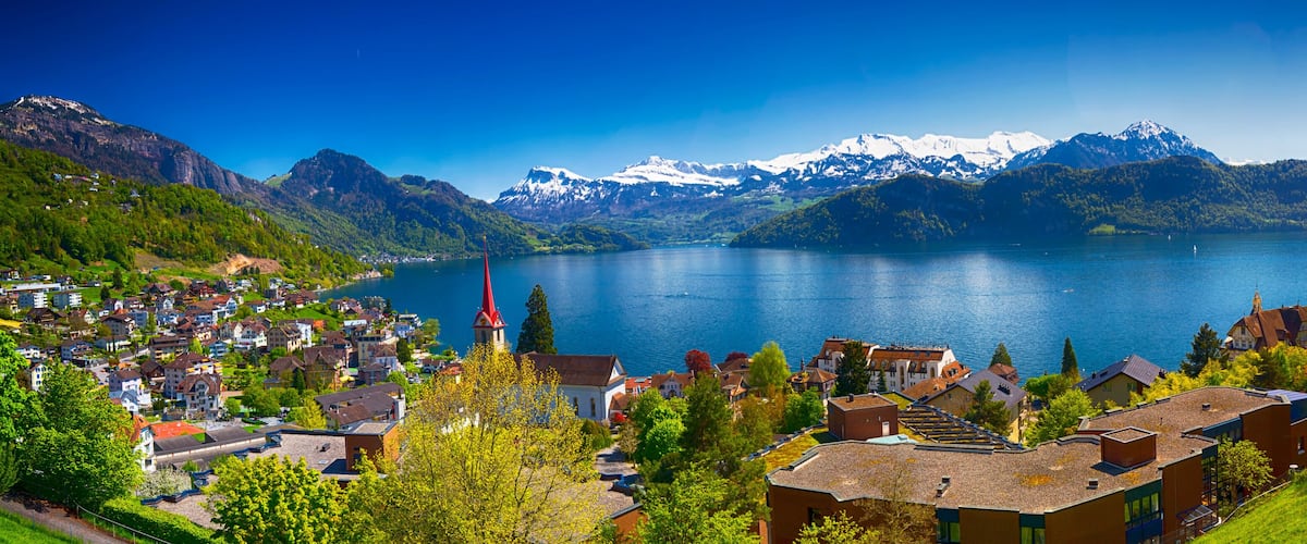 A lake surrounded by mountains and a town with a prominent church spire.