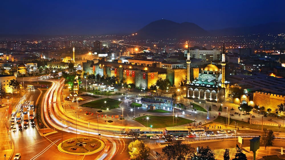 A cityscape at night with illuminated buildings, a roundabout, and a prominent dome structure.