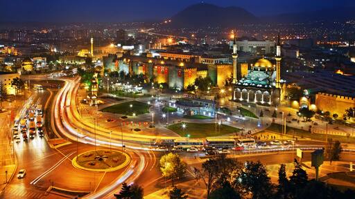 A cityscape at night with illuminated buildings, a roundabout, and a prominent dome structure.