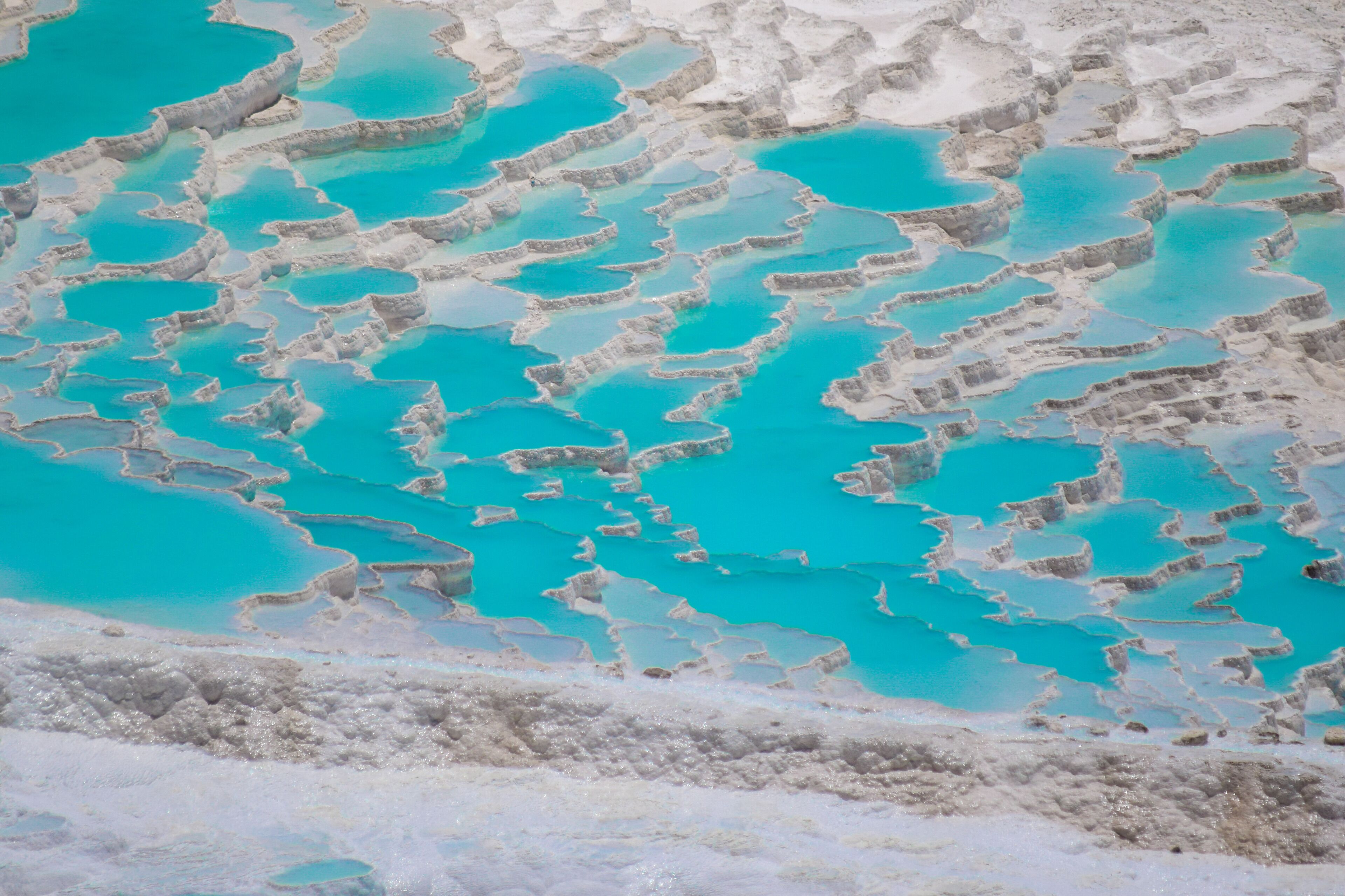 Piscinas escalonadas de color turquesa y formaciones minerales blancas.