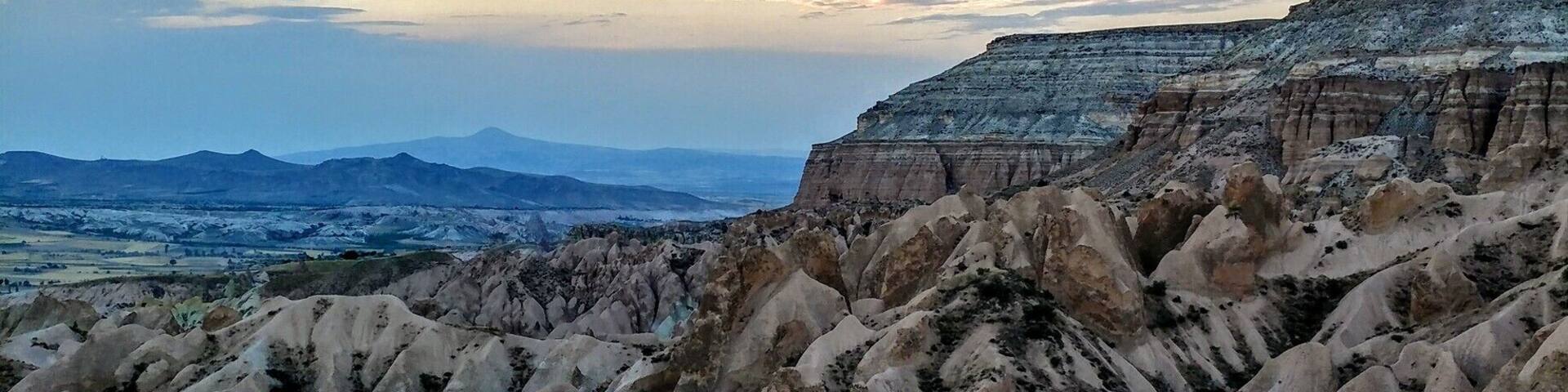 A rugged landscape with eroded rock formations and distant mountains under a clear sky.