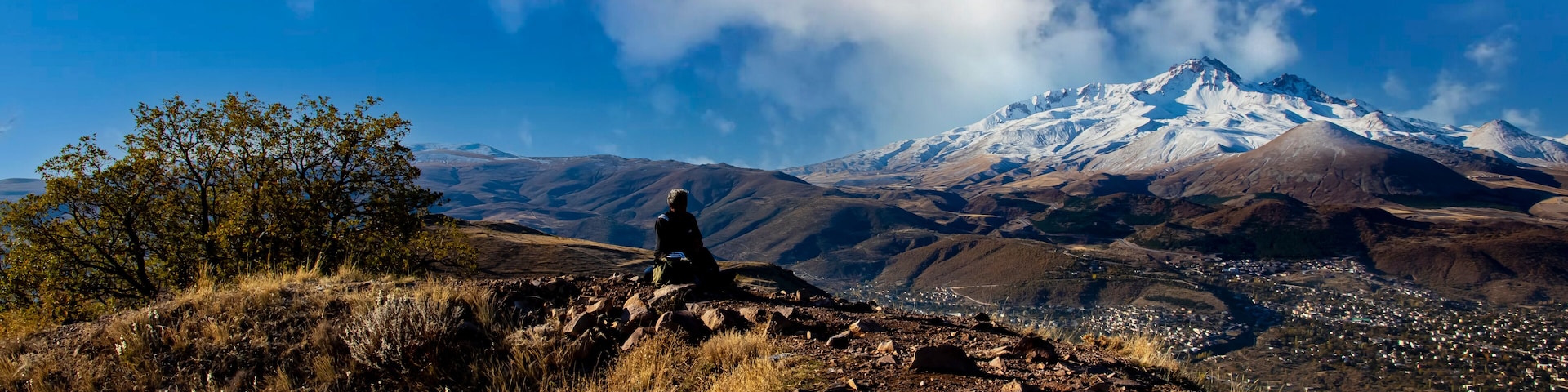A person sitting on a rocky outcrop with a snow-capped mountain in the background.