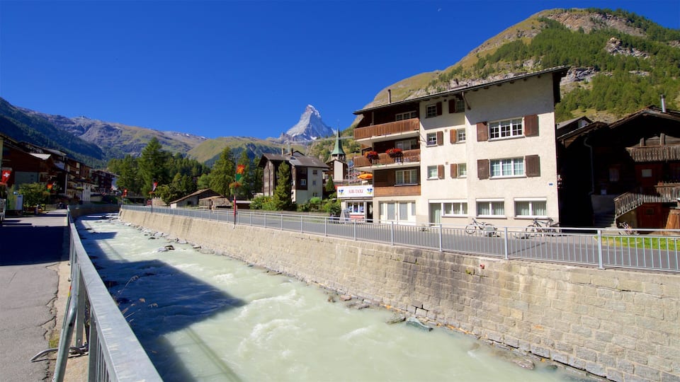 A river flowing through a town with buildings and mountains in the background.