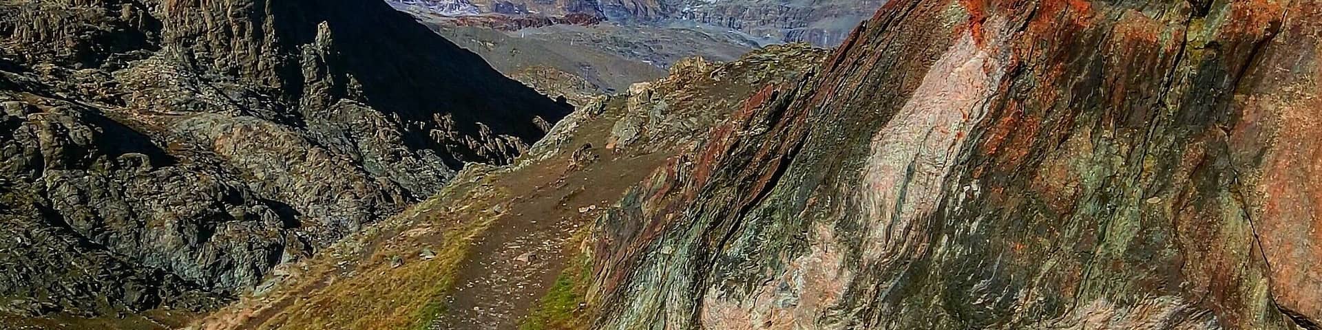 A mountain path leading to a snow-capped peak with rugged terrain on either side.