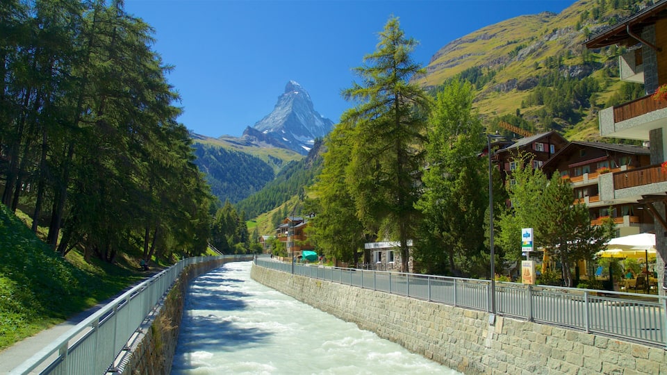 A river flowing through a mountainous area with a bridge and buildings on the right.