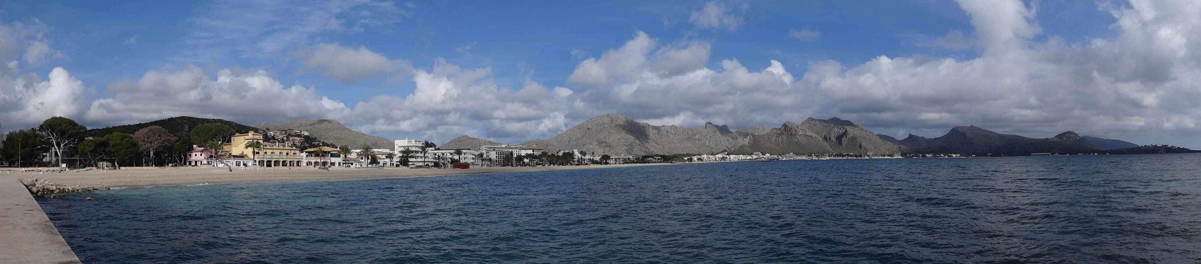 A coastal town with a beach, buildings, and mountains in the background.