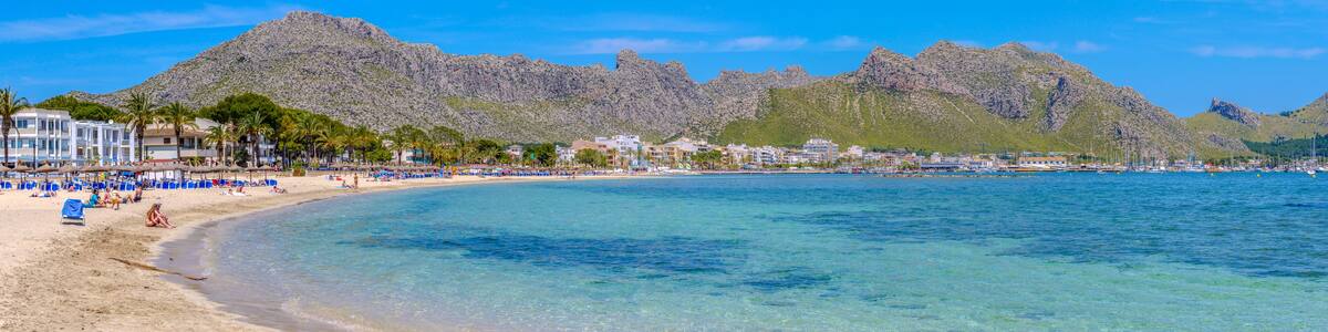 Ein Strand mit klarem türkisblauem Wasser, Palmen und felsigen Bergen im Hintergrund.