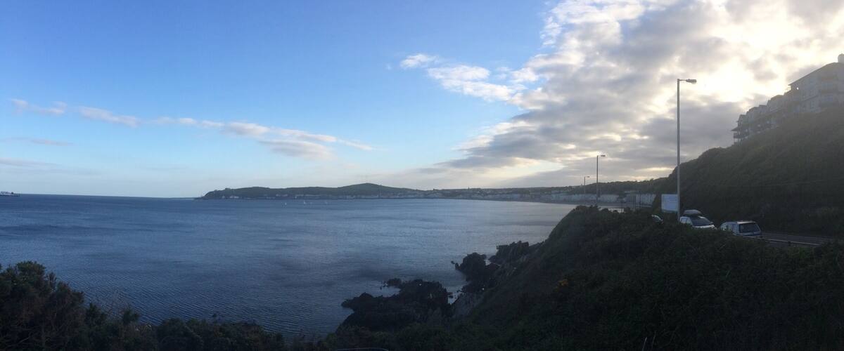 A coastal landscape with a clear sky, calm sea, and a road with parked cars.