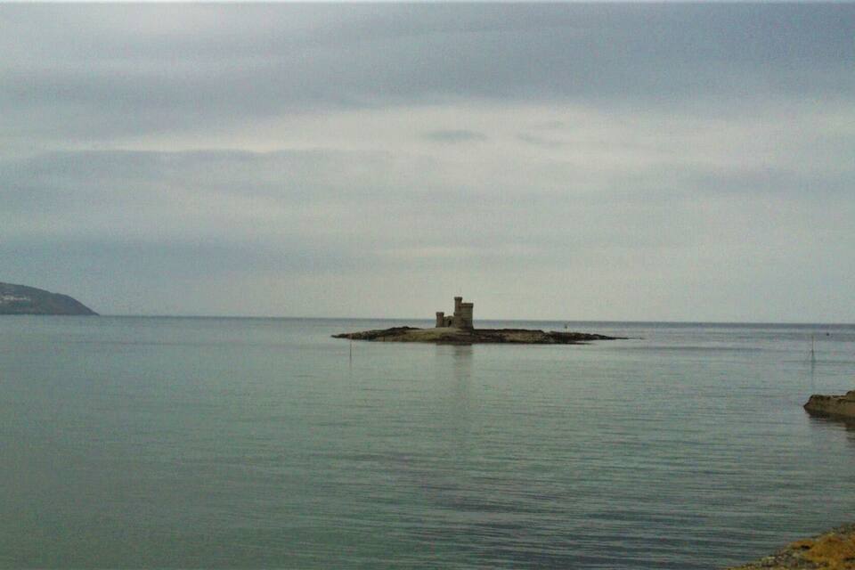 Una pequeña isla con una torre en medio de un mar tranquilo.