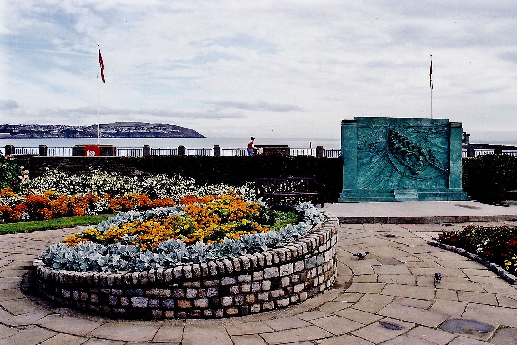 Douglas - Loch Promenade - Gardens, Memorial View is to the north from Loch Promenade, southeast of Regent Street. A lifeboat memorial is shown at the near right and Onchan Head is shown in the distant north at the left.