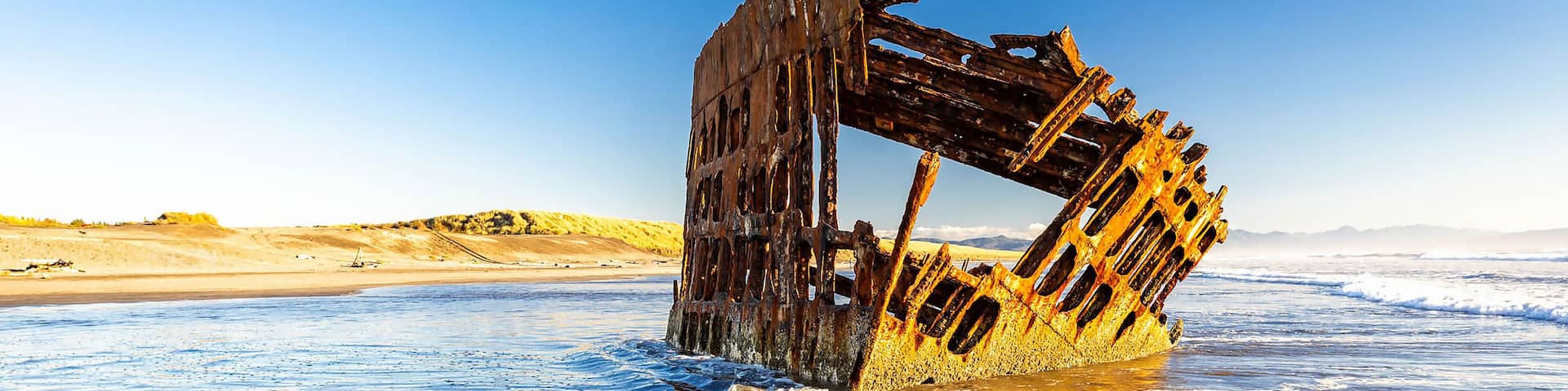 A rusted shipwreck in the ocean with clear skies.