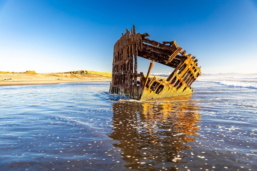 A rusted shipwreck in the ocean with clear skies.