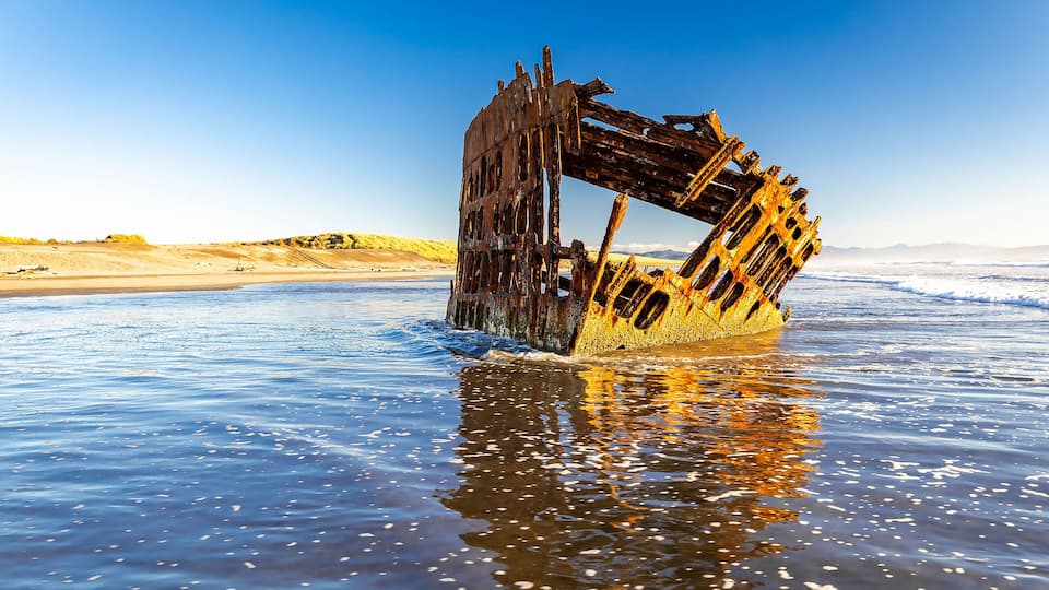 A rusted shipwreck in the ocean with clear skies.