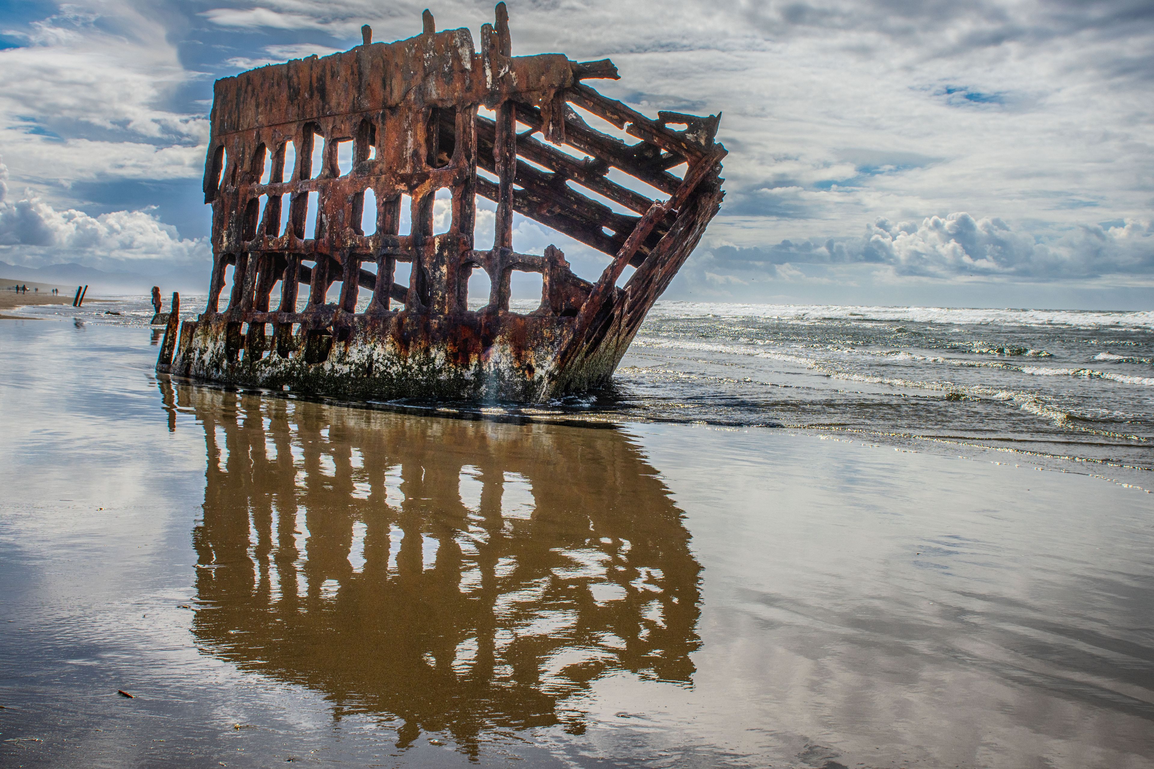 A rusted shipwreck on a beach with waves crashing around it.
