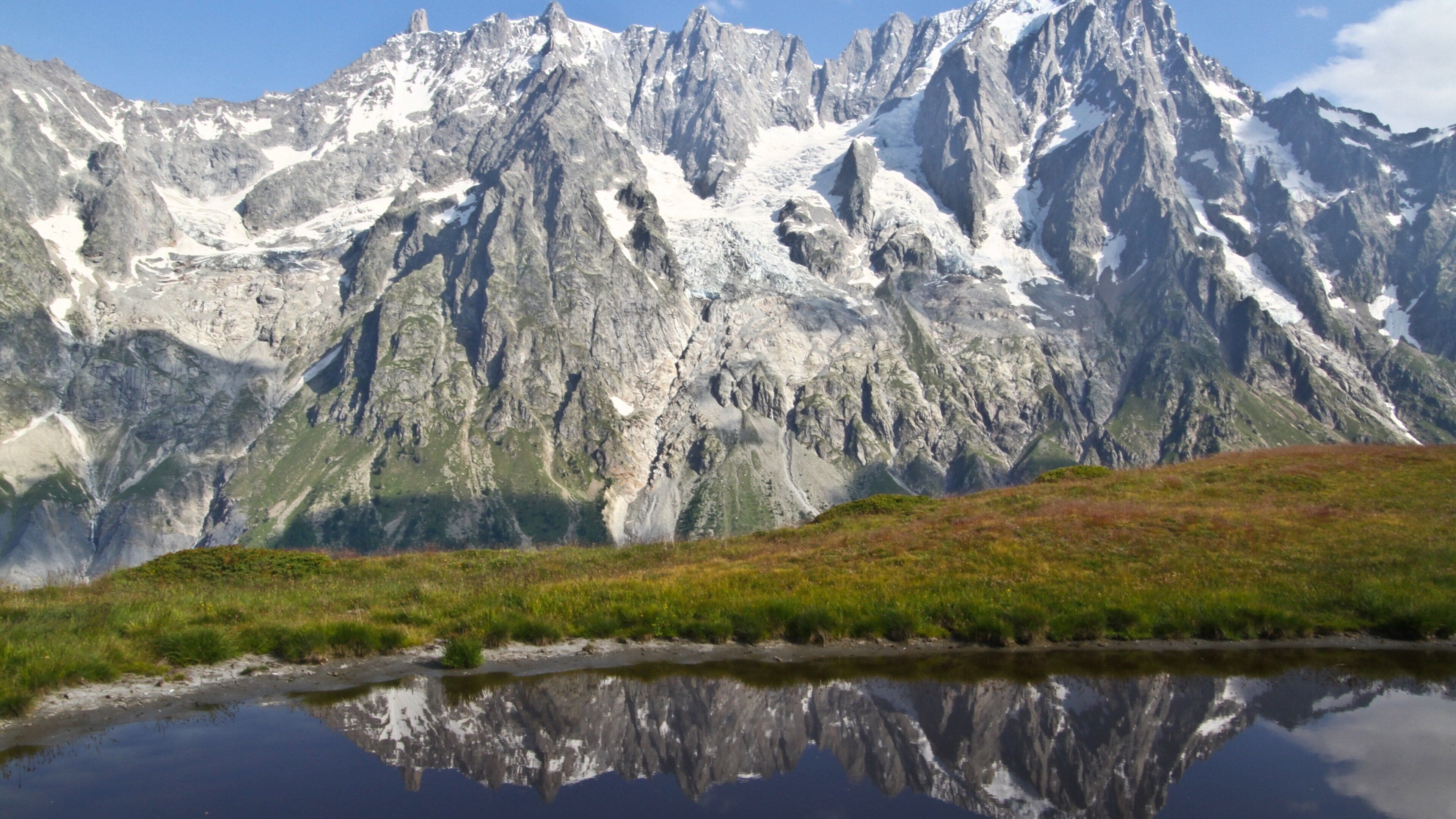 A mountain range with snow-capped peaks and a lake reflecting the scenery.