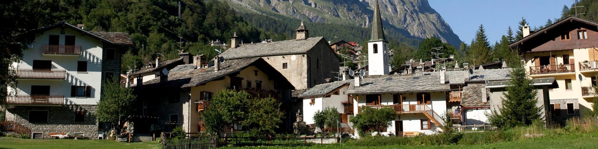 A mountain village with traditional buildings and a church, surrounded by snow-capped peaks.