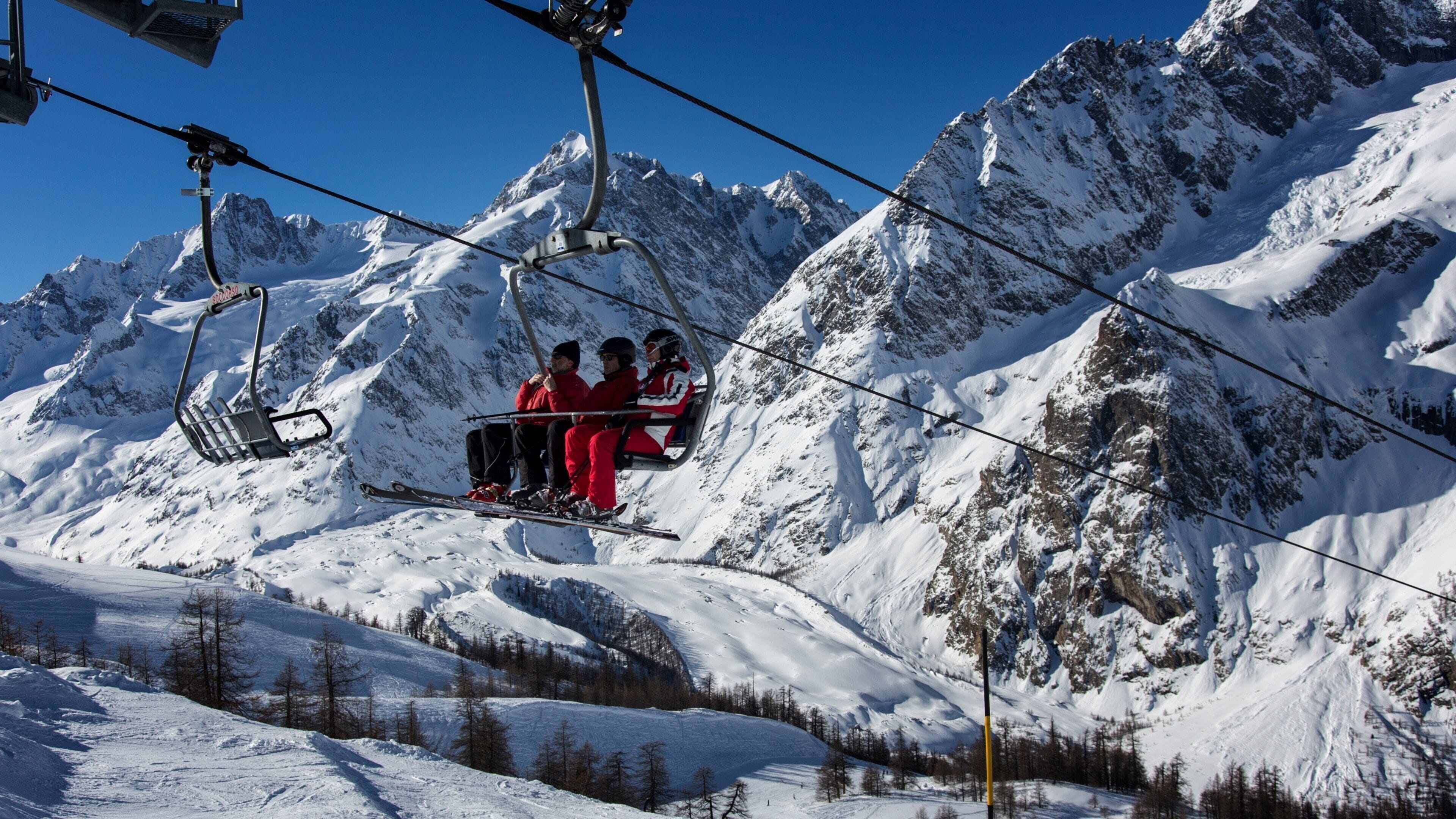 A ski lift with skiers in red jackets ascending a snowy mountain.