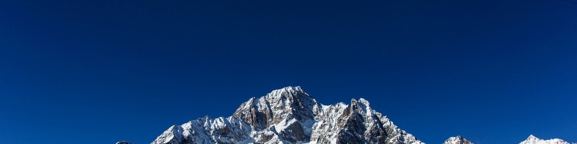 Un teleférico asciende un pico montañoso cubierto de nieve bajo un cielo azul despejado.