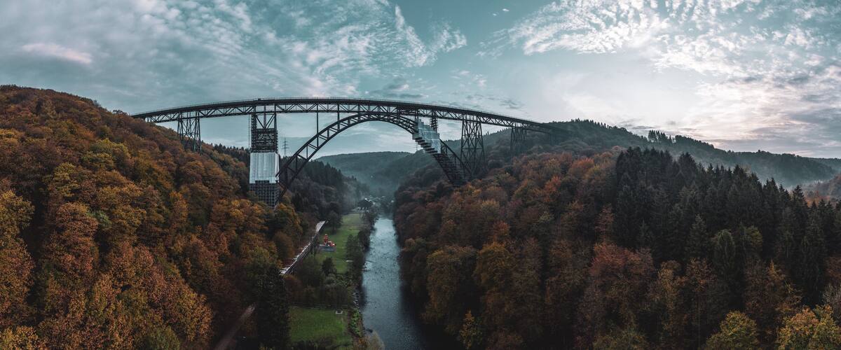 A steel bridge spanning a river, surrounded by autumn-colored forest.