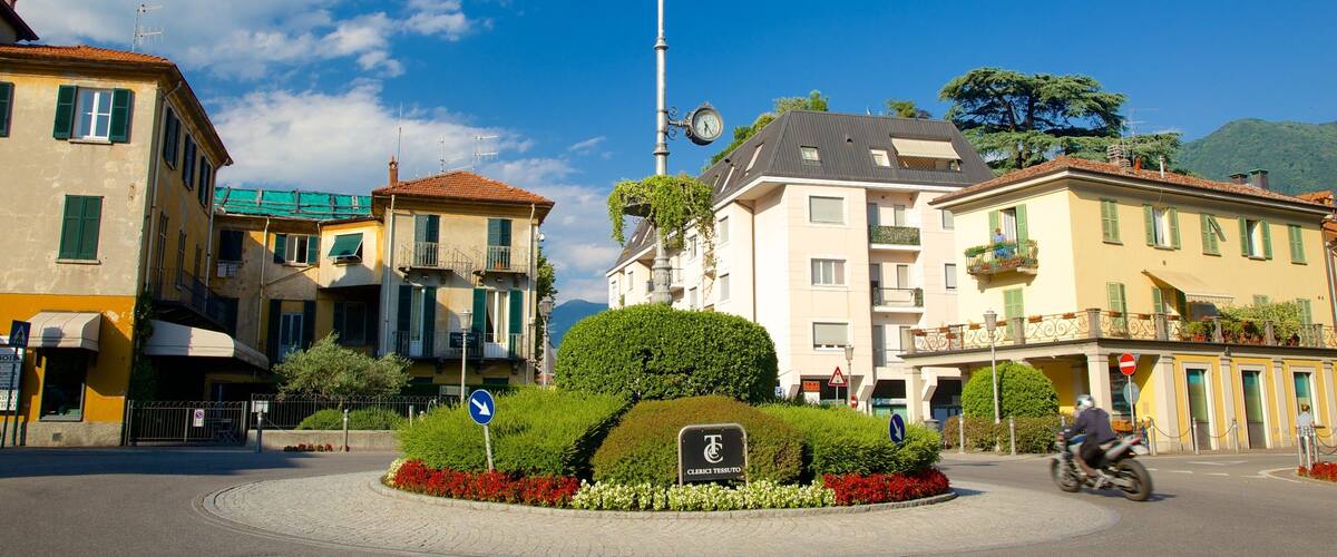 A roundabout with a clock tower, surrounded by buildings with green shutters, and a clear blue sky.