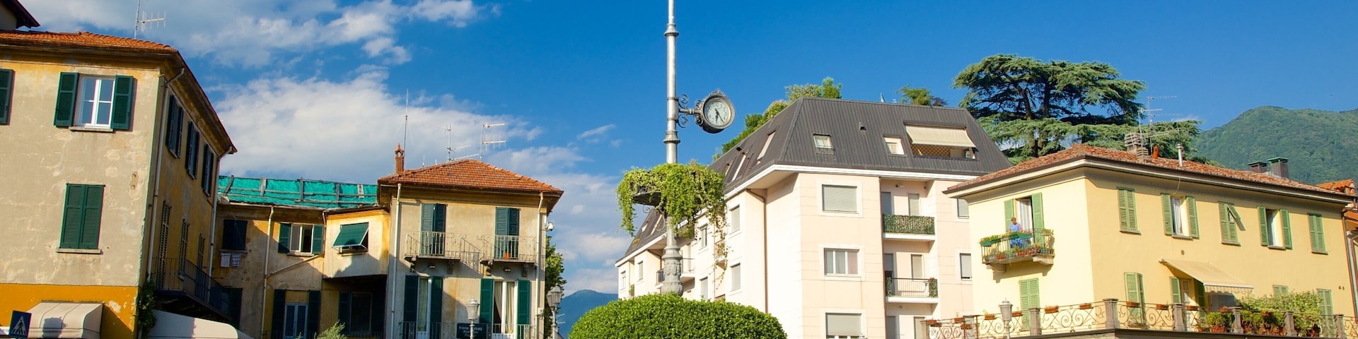 A roundabout with a clock tower, surrounded by buildings with green shutters, and a clear blue sky.