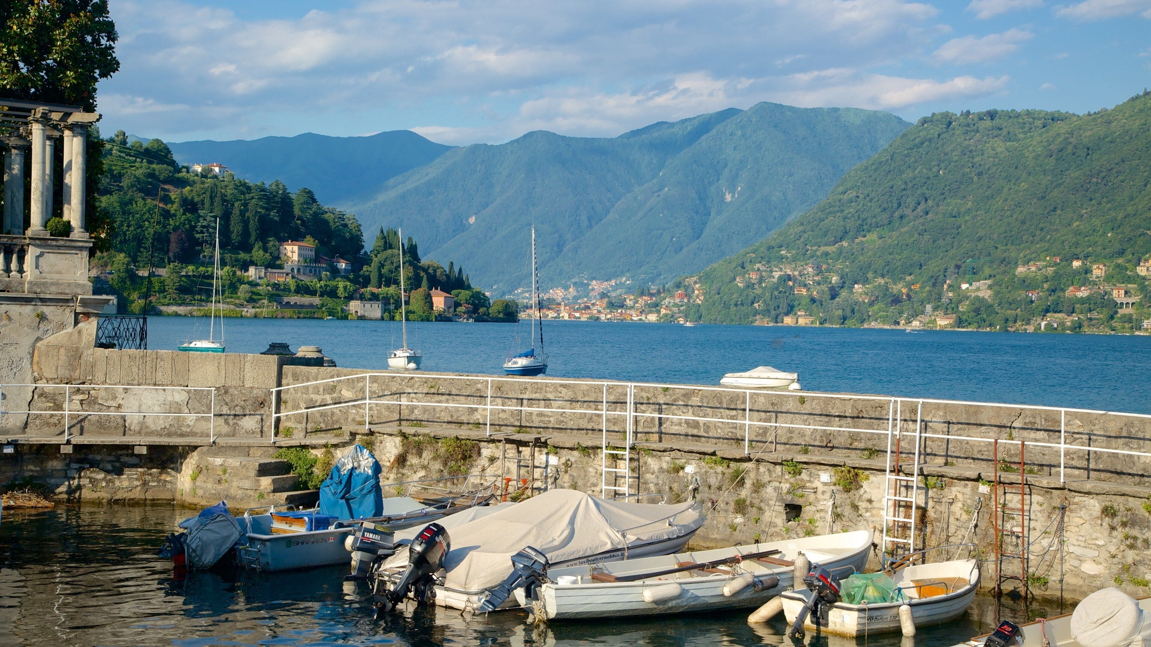A harbor with boats, a stone wall, and mountains in the background.
