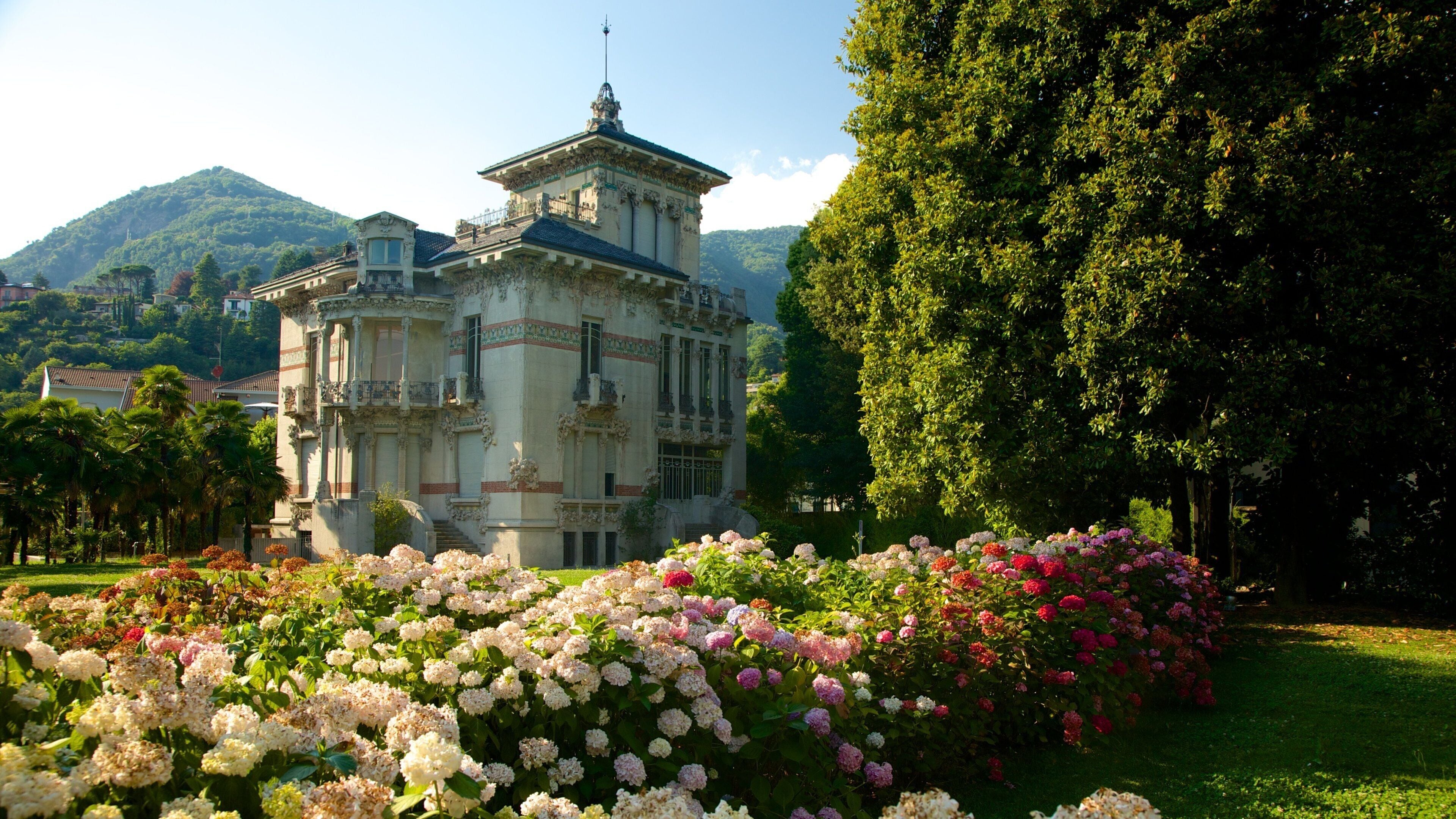 A historic building with ornate architecture, surrounded by lush gardens and a mountain backdrop.