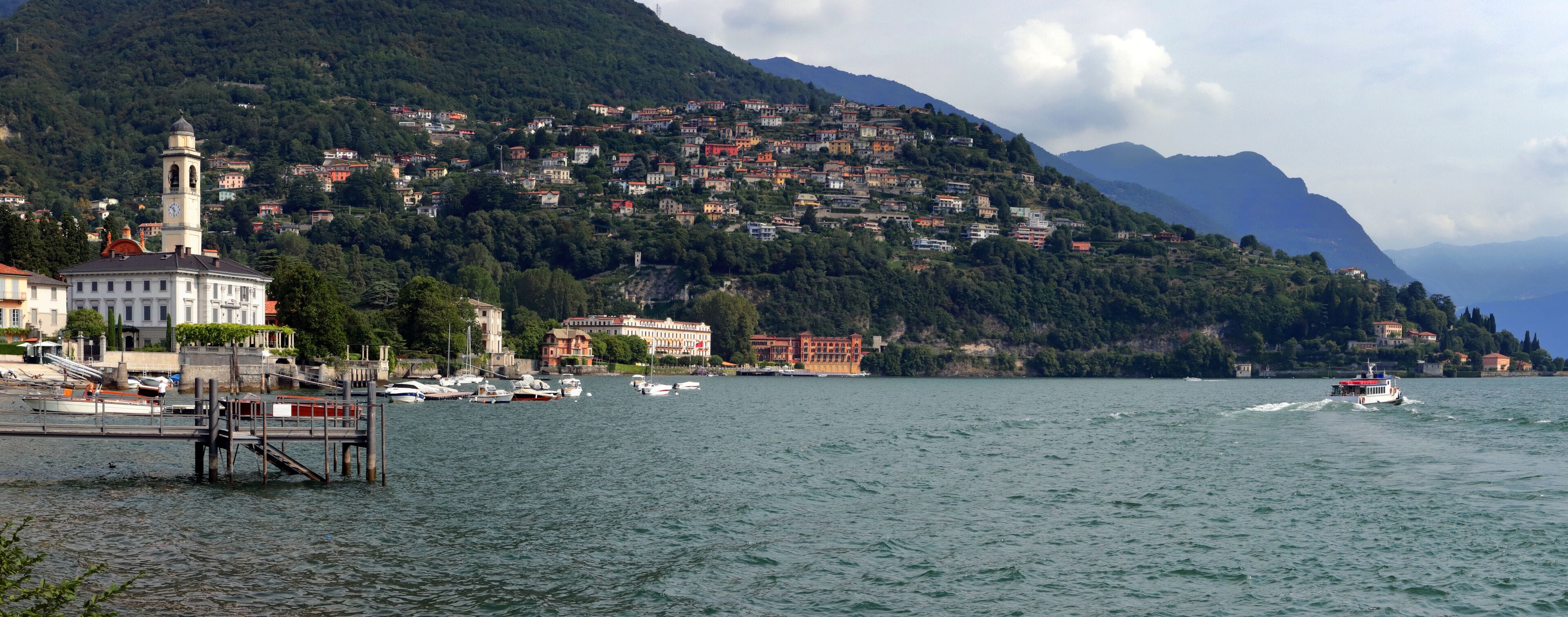 A coastal town with a prominent clock tower, a dock with boats, and a mountainous backdrop.