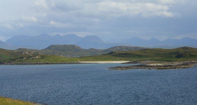 A coastal landscape with a body of water, grassy hills, and distant mountains.